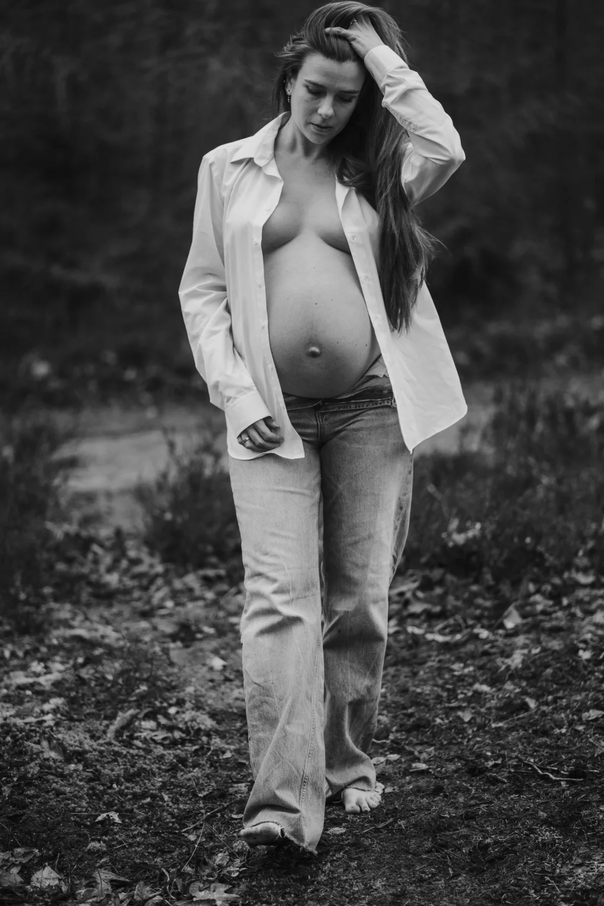 Klassiek portret van zwangere vrouw waarvan benen en buik te zien zijn borsten verscholen onder witte oversized blouse in de natuur.