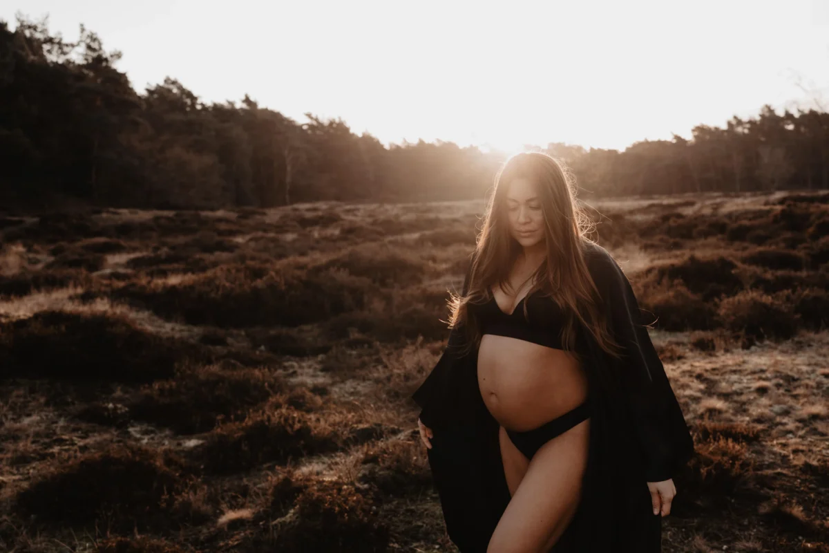 warme kleuren van de avondzon tekenen het landschap en de huid van deze zwangere vrouw in zwarte lingerie met zwarte kimono aan.