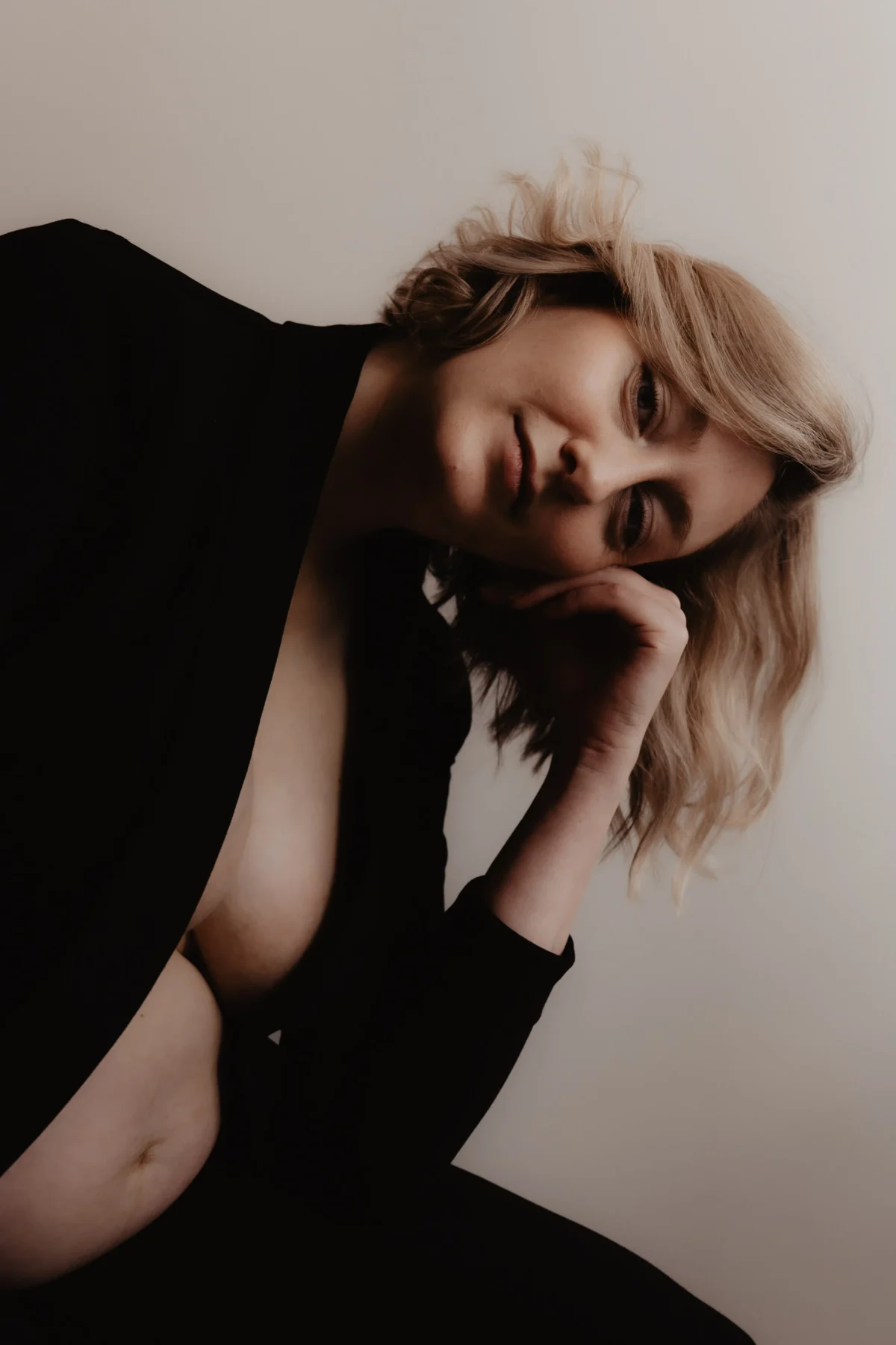 Portret van mama to be met open zwarte blazer zacht leunend op hand met ogen dicht, kort blond haar, zachte maar krachtige uitdrukking