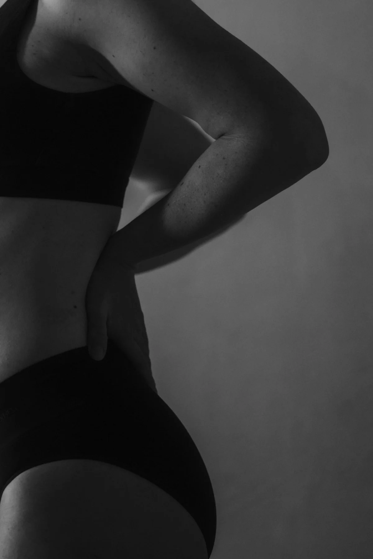 Boudoir fotografie van een vrouw met lingerie waarvan je de rus, billen en armen ziet, natuurlijke schoonheid komt naarboven