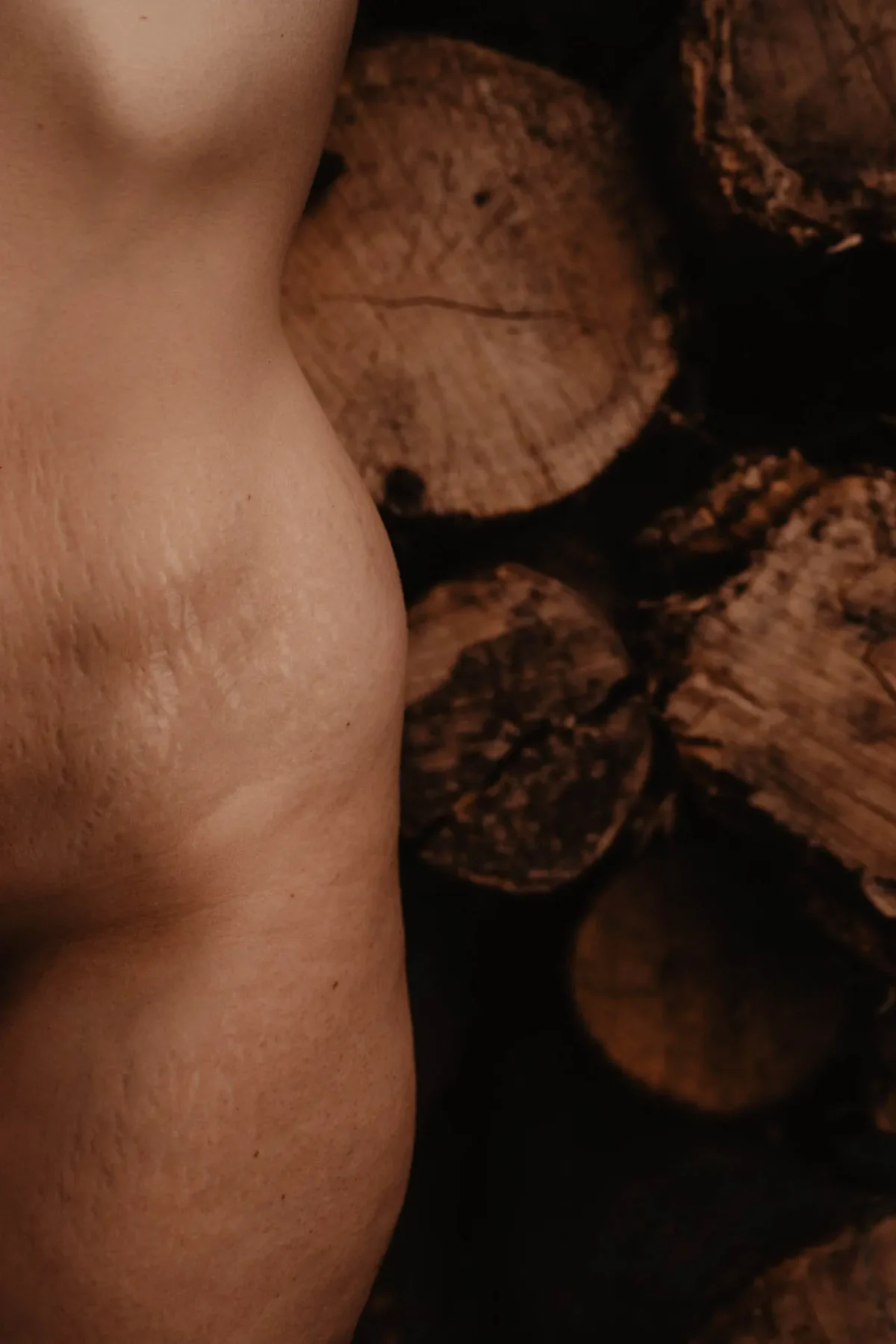 boudoir foto van een naakte vrouw die tegen hout aan leunt