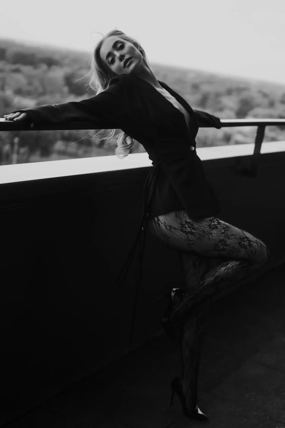 Vrouw leunt tegen balkon aan in strakke zwarte outfit die de contouren van haar lichaam mooi uit laten komen, ze ziet er voldaan en zelfverzekerd uit.