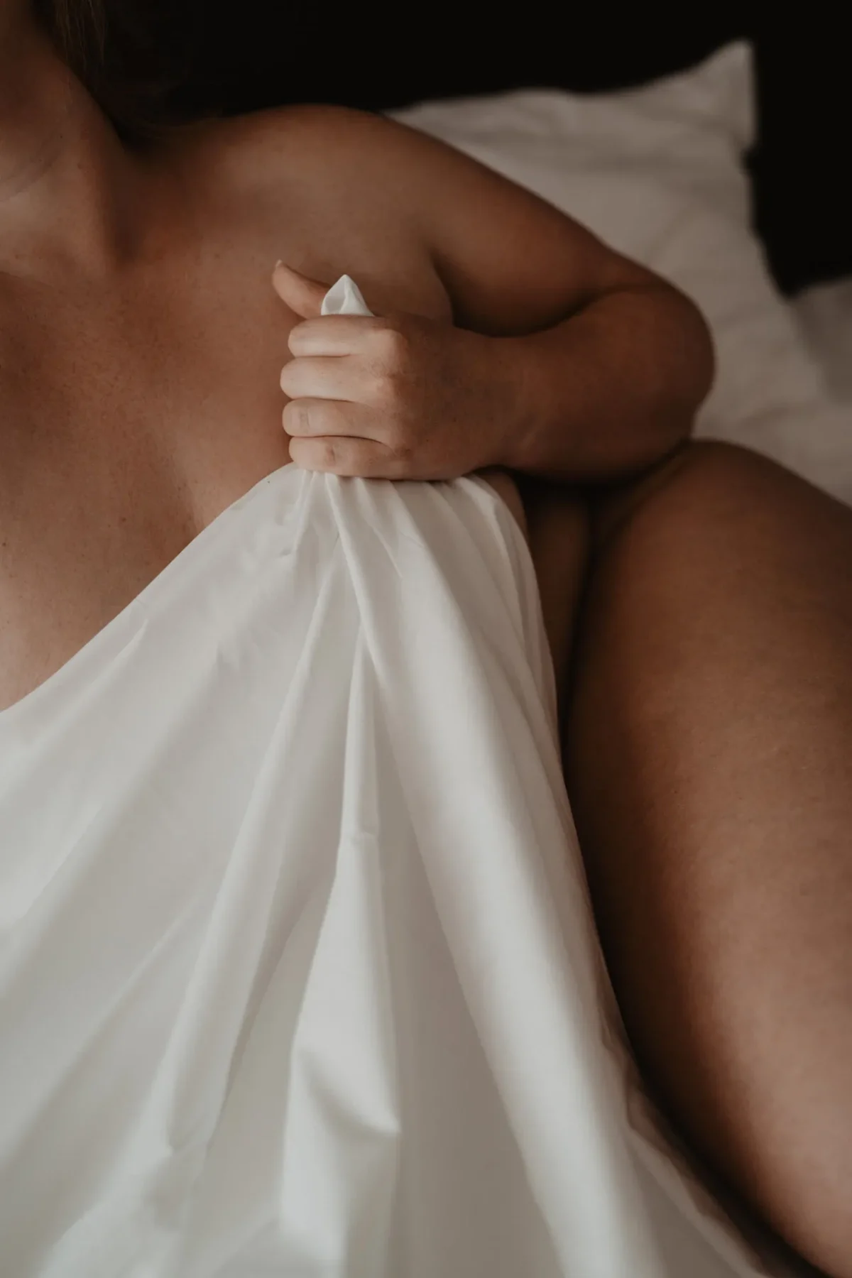 vrouw houdt laken voor borsten, de focus licht op haar huid en vormen.