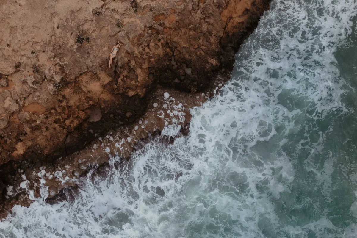 uniek shot van vrouw op rotsen van bovenaf te zien met een ruige zee die tegen de rotsen aanklettert