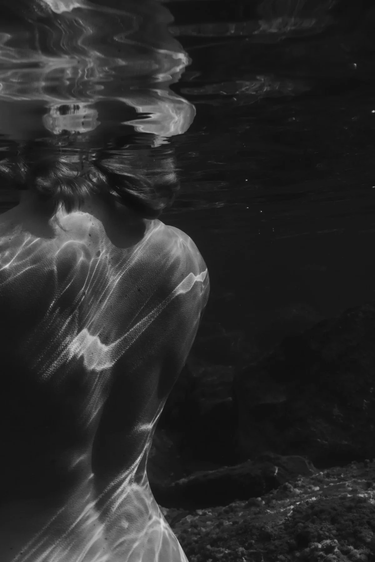 kunstzinnige foto van vrouw onderwater met clair obscur effect, enkel de schouders komen uit het donker tevroorschijn.