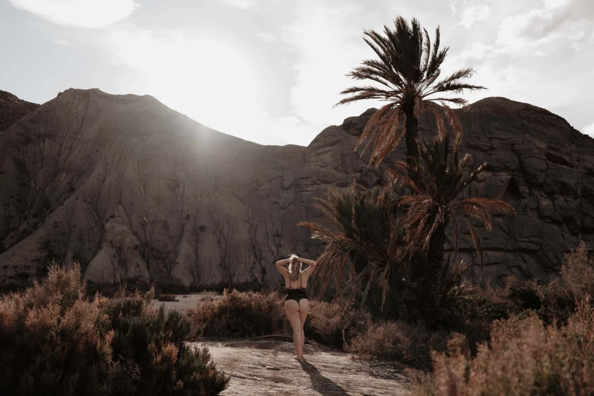 vrouw loopt door een soort oase achtig landschap met armen in het haar.