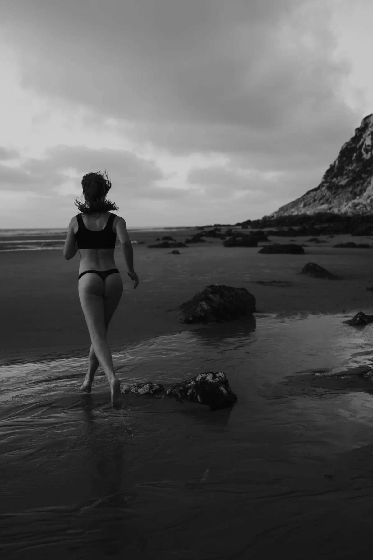 Vrouw rent over strand, van achteren te zien, zwart-wit, avondzon.