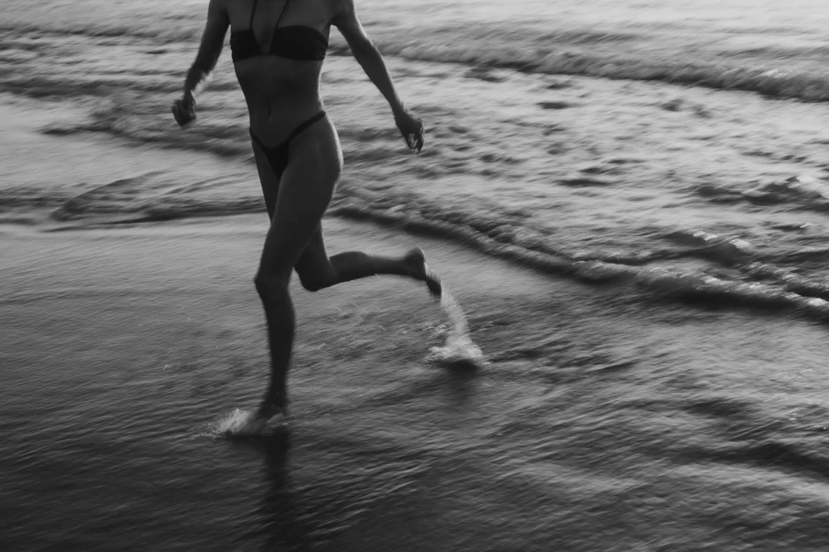 onderlichaam te zien van vrouw die in de branding rent, zwart-wit, artistiek licht.
