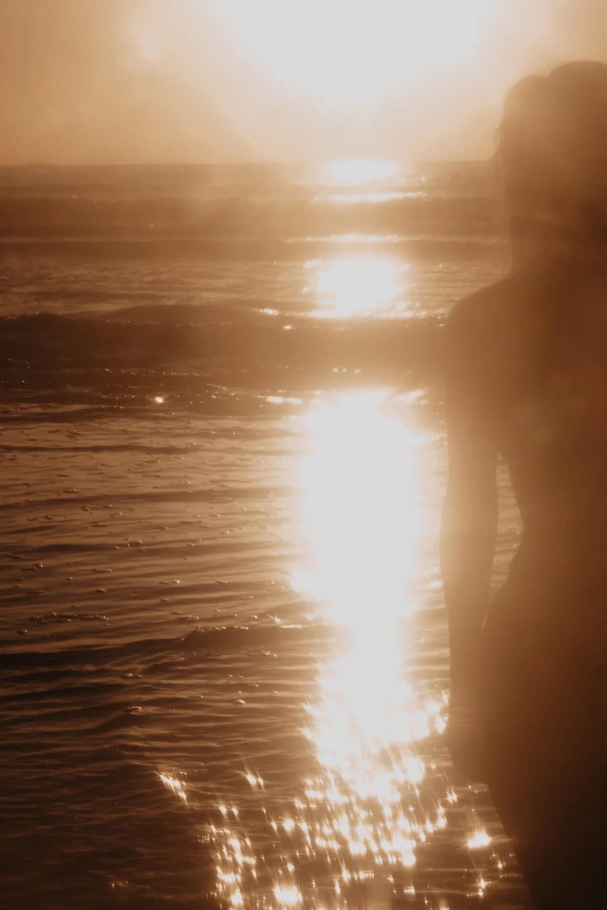 zonsondergang met overbelichting van zonlicht in de lens met aan de rechter kant een vrouw van wie je nog net de arm ziet voor een artistiek zonovergoten gouden beeld.