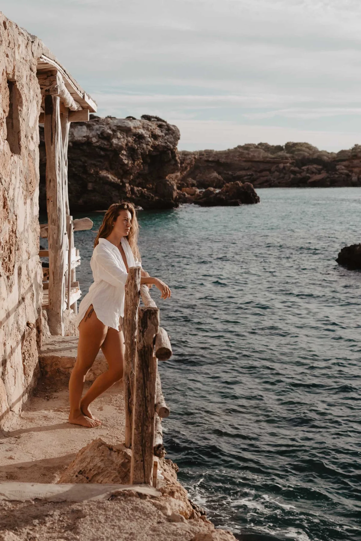 Klassiek Ibiza vibe kust gezicht met vrouw in witte blouse die uitkijkt over het water.