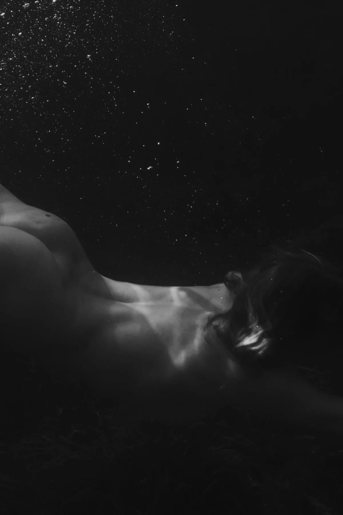 kunstzinnige foto van een vrouw die onder water duikt in zwart-wit waarvan de holling van de rug goed te zien is