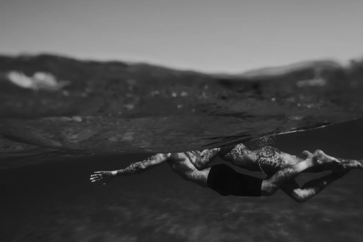 koppel dat samen zwemt op artistiek zwart-wit beeld waarbij hun hooft niet te zien is om dat de kamera de waterlinie van een golf heeft geschoten precies op die plaats.