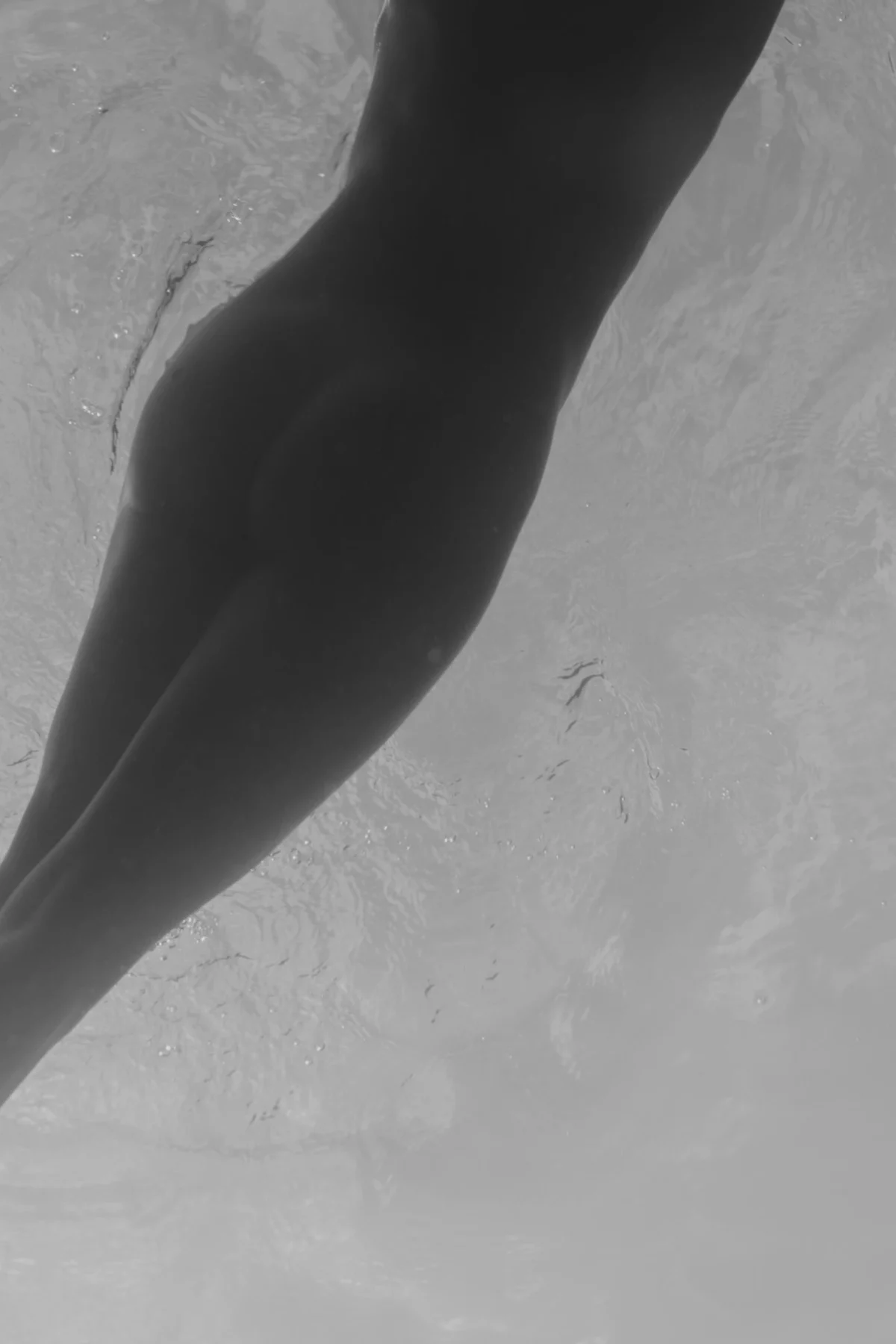 tijdloos portret van vrouw die onderwater is in een zwart-wit opname waarin haar billen en benen in zacht licht artistiek uitkomen als een vis in het water