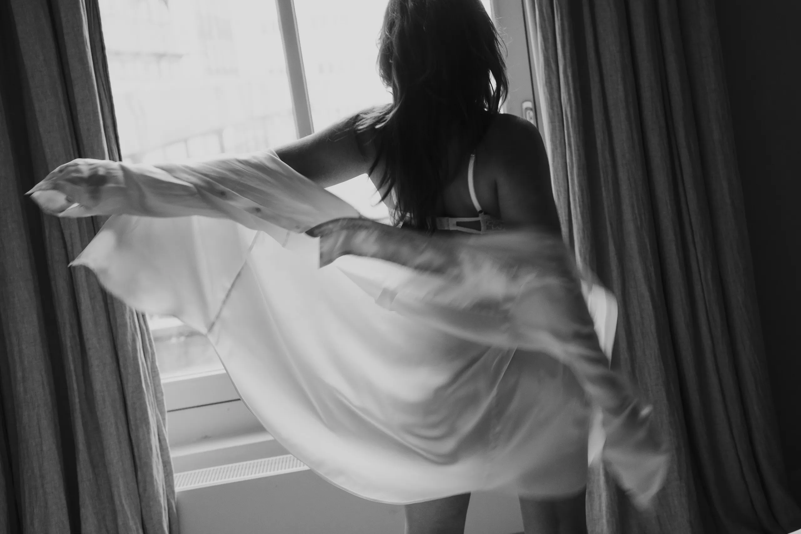 vrouw voor een raam bij boudoir shoot met witte blouse als outfit