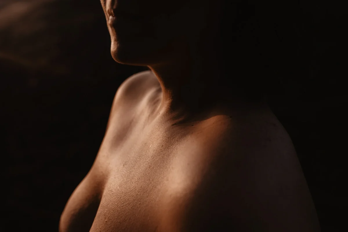 Artistiek beeld van torso van vrouw met glooiende warme bruine huid in het warme licht.