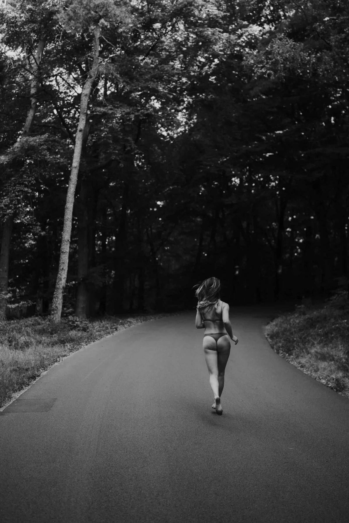 vrouw rent naakt door het bos op de weg met alleen een onderbroek aan in zwart-wit