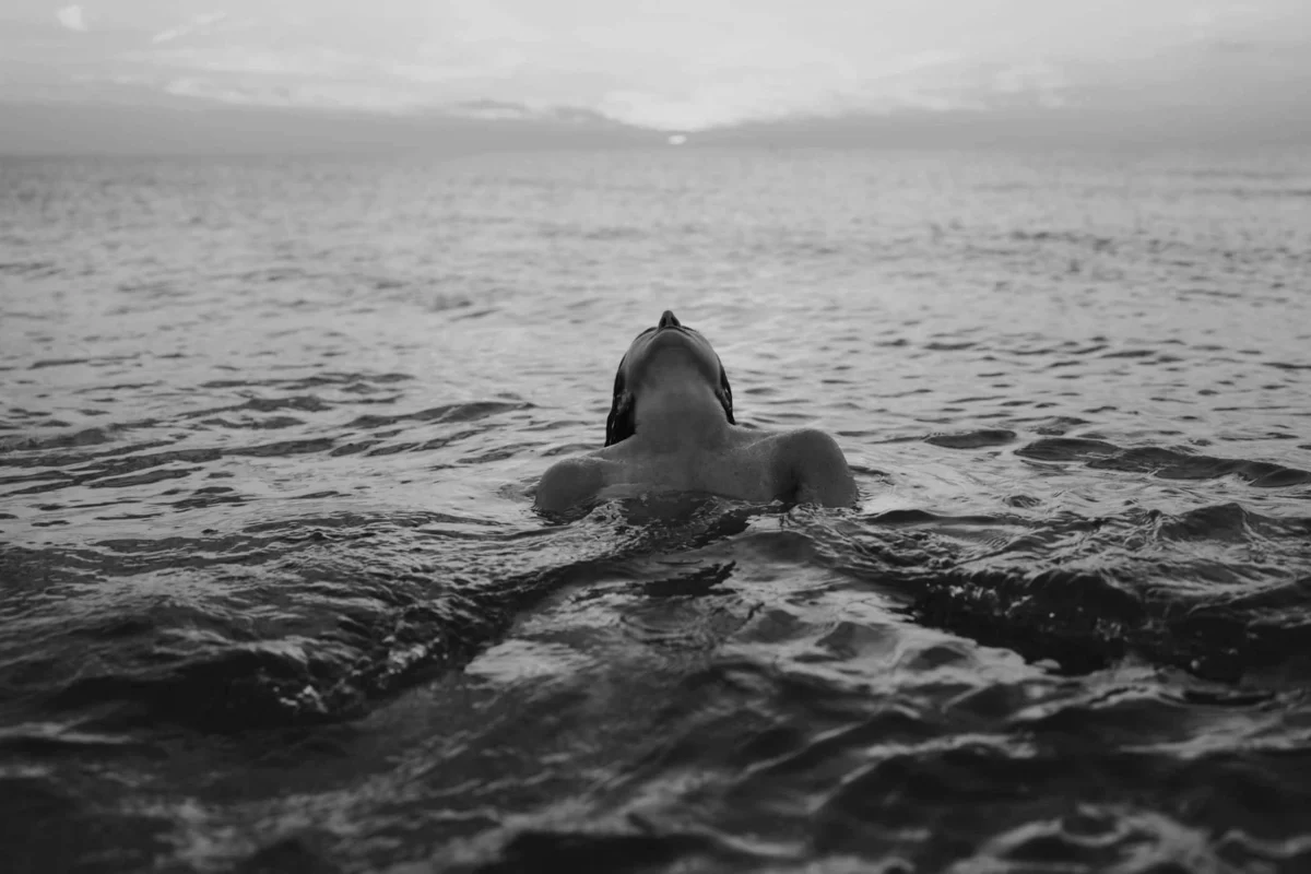 Portret gemaakt door de beste boudoir fotograaf van Nederland van vrouw die in het water ligt met hoofd naar achteren gebogen in een tijdloze zwart-wit foto waar haar kracht en schoonheid mooi uit komt.