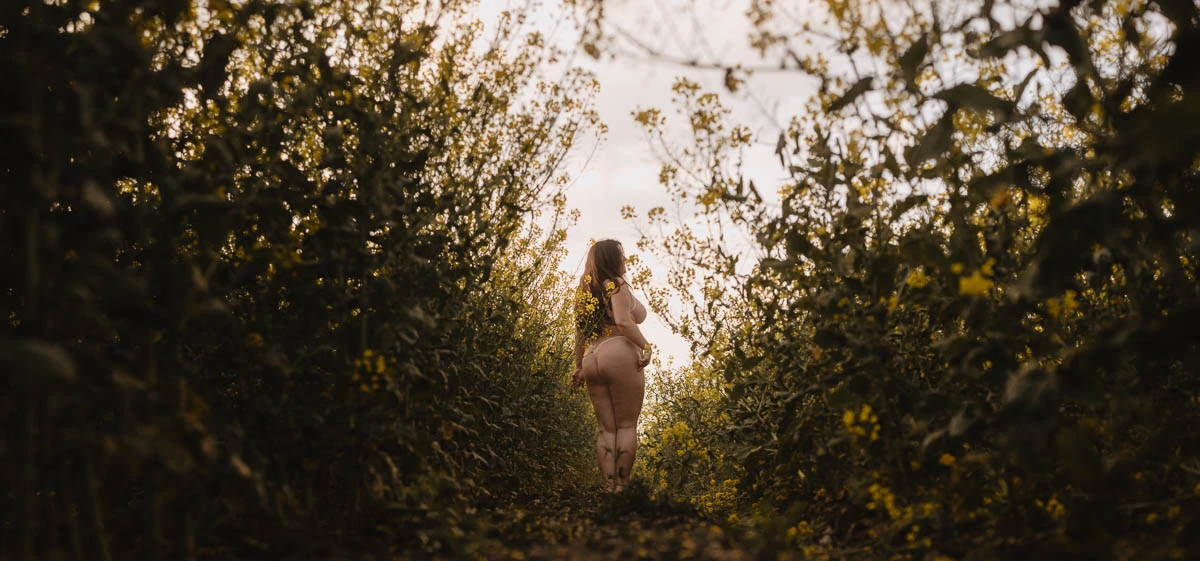 Vrouw tijdens boudoir shoot in bloemenveld in natuurlijke omgeving met warm avondlicht