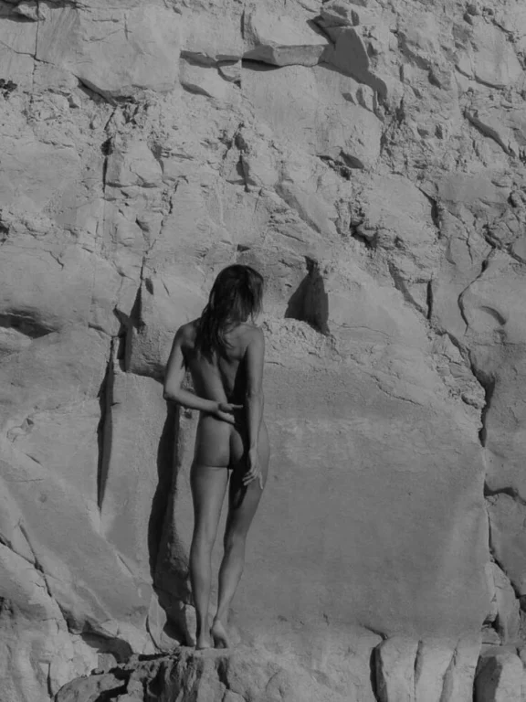 kunstzinnige zwart-wit foto van vrouw naakt van achteren te zien voor een rotspartij, ze blend in met het landschap, haar zachte vormen steken af tegen de ruigheid van de rots. Wat boudoir fotografie is, is hier te zien.